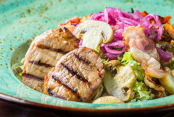 Grilled salad with pork: salad mix, bacon, pickled onions, mushrooms, tartar sauce on a turquoise plate. Side view