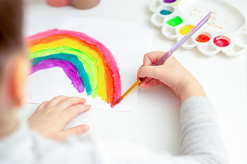 Hands of child receiving master class in paint drawing a rainbow by watercolors.