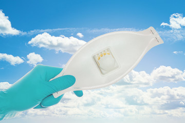 Hands in doctor gloves showing medical face mask against sky clouds background, safety and virus protection concept