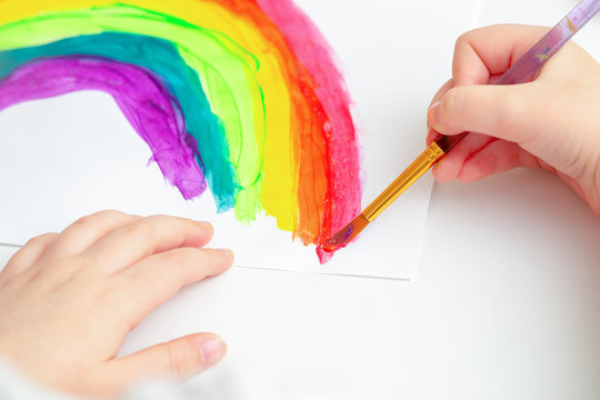 Hands Of Child Drawing Colorful Rainbow By Watercolors On White Sheet Of Paper. Children's Creativity Concept.