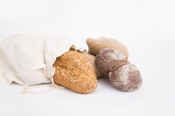 Buns and loafs of rye and wheat wholegrain bread in fabric bag. Closeup shot. Isolated object on white background. Food or bakery concept