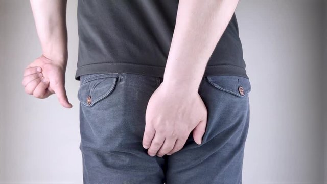 A man holds his hands to the ass feeling pain. Conversion of pain in the rectum, hemorrhoids and pain in the excretory system of the body. Frequent bowel movements.