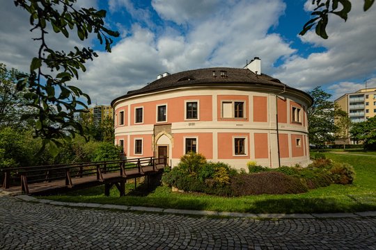 Prague / Czech Republic - May 12 2020: View of Chodov fotress with yellow and red facade standing in a park with green lawn and trees. Sunny spring day with blue sky and white clouds. 