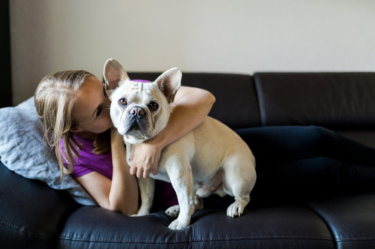 Woman is sitting with french bulldog on couch