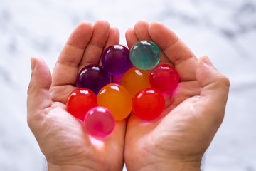 Photo of a hand holding a group of multicolored big polymer water balls that grow when you submerge them on water during a few hours