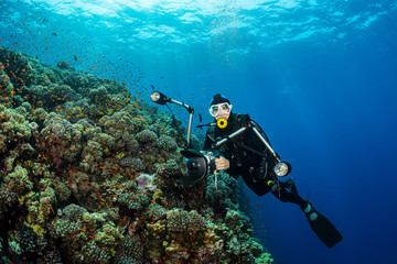 typical Red Sea tropical reef with hard and soft coral surrounded by school of orange anthias and a underwater photographer diver
