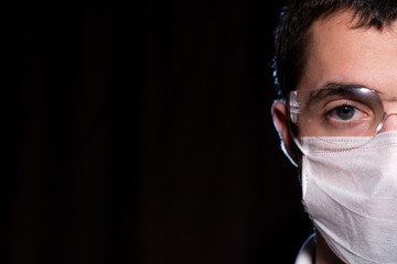 Concept photo half face of a young man wearing mask and goggles on black background. Young doctor in medical mask and goggles. Protective mask and goggles on handsome man