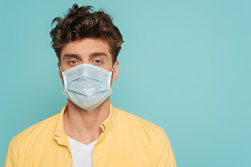 Portrait of man in medical mask looking at camera isolated on blue