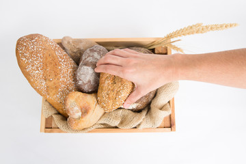Hand taking French loaf from box with homemade rye and wheat bread and ears. Top view. Isolated object on white background. Baking or traditional bread concept