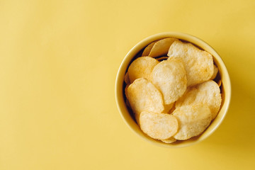 Potato chips in a yellow bowl on a yellow background. Top view. Copy, empty space for text