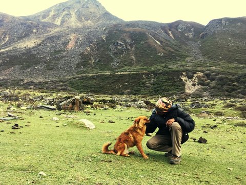 Man Looking At Dog On Field Against Mountains