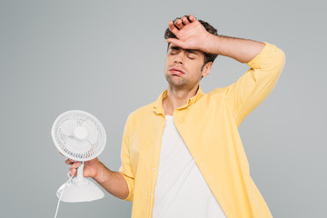 Man with desk fan suffering from heat isolated on grey