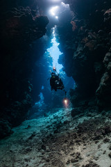 Naklejka na ściany i meble typical underwater cave in a red sea reef with an underwater photographer diver