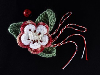 Handmade crocheted flower on black background and red and white string, known as Martisor. It is a...