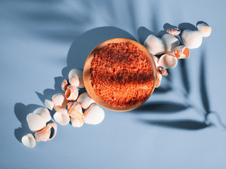 Orange bath salt in a saucer with shells on a blue background with a shadow from a tropical plant....