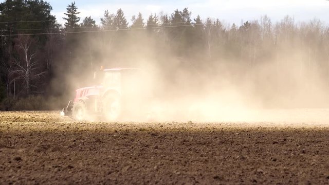 Side view of a tractor with a large reverse plow passing through dusty and arid farmland in hot weather. The concept of unprofitable agribusiness. Low fertility and soil erosion