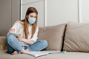 woman at home on couch wearing mask studying with books and notebook