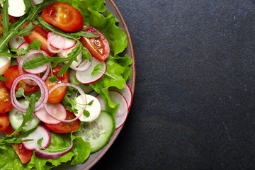 Healthy fresh salad with radish, cucumber, cherry tomato and mozzarella on a dark color background. The concept of a delicious and healthy diet.