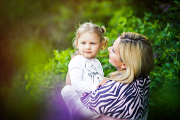 Lifestyle portrait blonde mom and daughter outdoors. Mother and child girl hugging and having fun outdoor in nature. Woman looking on kid. Mother day. Love, trust, togetherness in family.