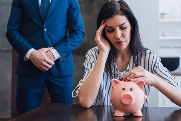 Upset woman touching piggy bank at table near collector with clenched hands