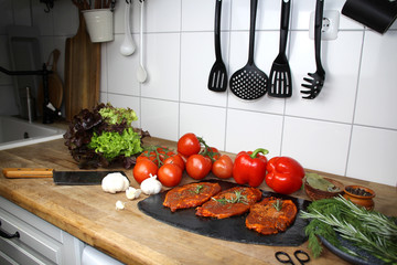 juicy marinated with spices raw meat on a black board in the kitchen, steaks with rosemary, red tomatoes, paprika, garlic, salad, concept of protein nutrition, barbecue party, cooking homemade food