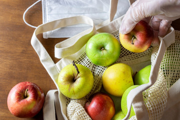 Hand in glove holds apple. Eco mesh bag with food supplies on a wooden background. Food delivery in eco-friendly packaging, zero waste.