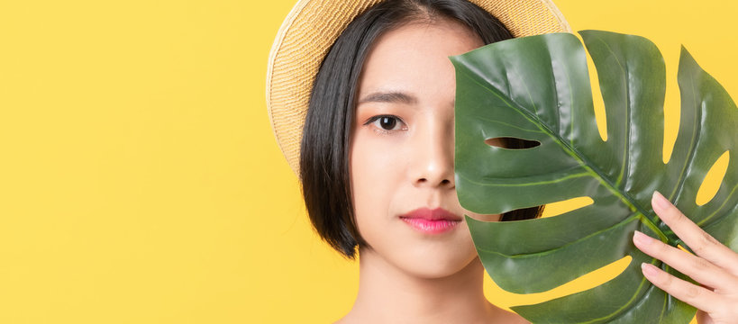 Beauty Shot Of Asian Woman Holding Green Leaves To Touch The Face On The Orange Background.