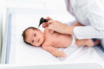 Pediatrician examines 2 week old baby's ear in new pediatric clinic. Young doctor using otoscope...