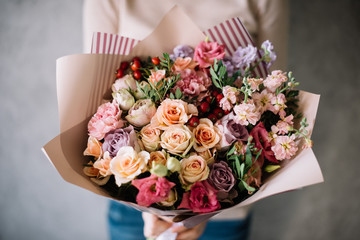 Very nice young woman holding big beautiful blossoming bouquet of fresh hydrangea, roses, eustoma flowers in burgundy and pink colors on the grey wall background