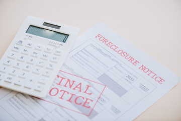 High angle view of foreclosure and final notice lettering with calculator on white