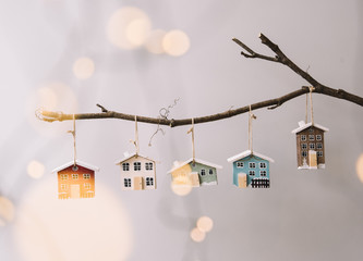 Beautiful festive new year and Christmas decorative little wooden houses hanging on a stick on the grey wall background, with fireflies glowing on the foreground