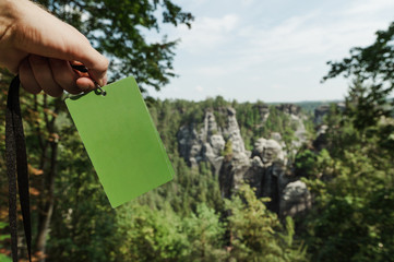Green card in men's hands on the background of Saxon Switzerland National Park, Germany. Man holding. in the hand of a tourist guide on a background of rocky mountains on untouched nature