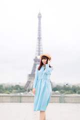 Cheerful smiling woman tourist at Eiffel Tower smiling and posing to camera. Beautiful European girl enjoying vacation in Paris, France