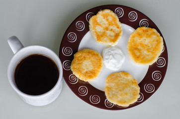 Cheese pancakes or syrniki (cheesecakes, curd fritters) with sour cream or smetana and cup of coffee for breakfast