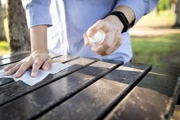 Hand of woman is spraying alcohol,wiping the dirt,disinfectant spray on table,during the pandemic of Covid-19,Coronavirus,cleaning,disinfecting wipe the public wooden table at park,hygienic for safety