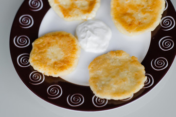 Cheese pancakes or syrniki (cheesecakes, curd fritters) with sour cream or smetana for breakfast