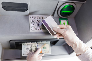 Customer wearing medical gloves and withdrawing money from credit card at atm machine outdoors. Coronavirus concept.