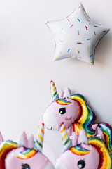 Adorable inflatable unicorn balloons with the pink mood and a star balloons on the grey wall background, vertical photo