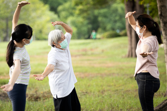 Happy Family Smiling While Exercising At Outdoor Park,mother,daughter And Healthy Grandmother Are Stretching Arm Workout,wearing Surgical Mask,enjoy,relaxation After Coronavirus Quarantine Or Covid-19