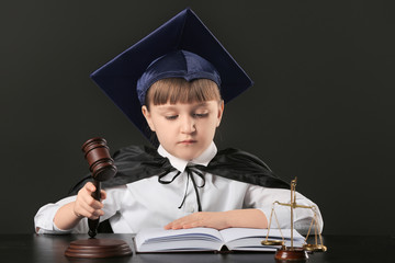 Portrait of little judge sitting at table against dark background