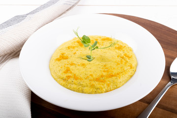 Mixed vegetable cream soup in a white bowl, isolated on a white background, on wooden cutting board