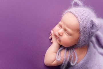 newborn baby girl. the newborn is lying on a purple background in a knitted hat with ears