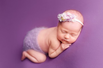 newborn baby girl. the newborn is lying on a purple background. newborn girl in a flower wreath