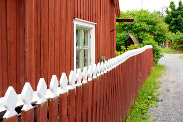 Traditional red wooden house in the island of Sweden decorated with frence wood paint in white on top on green leaves over sky background in summertime.
