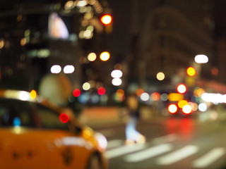 Defocus blur of New York City street scene at night with yellow taxi cabs, cars, lights and buildings.