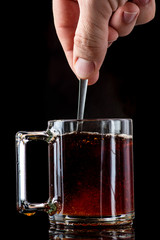 dissolving and stirring sugar in tea in a transparent mug on a black background