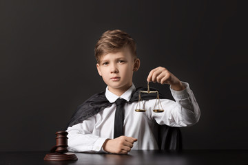 Portrait of little judge sitting at table against dark background