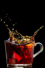 splash and spray of tea in a transparent mug on a black background