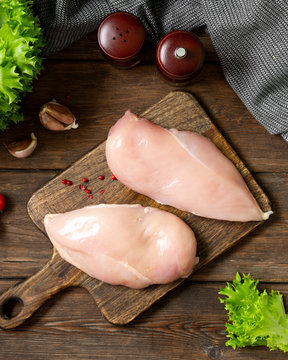 Chicken breast fillet on a wooden Board on a brown wooden table. Raw chicken breast. Top view with space for text