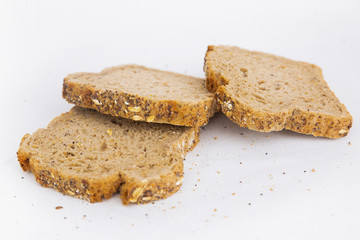 Three slices of brown bread with oats. Crumbs laying around. Healthy rye loaf sliced pieces isolated on white background. Studio shot. Side view. Homemade food and nutrition concept